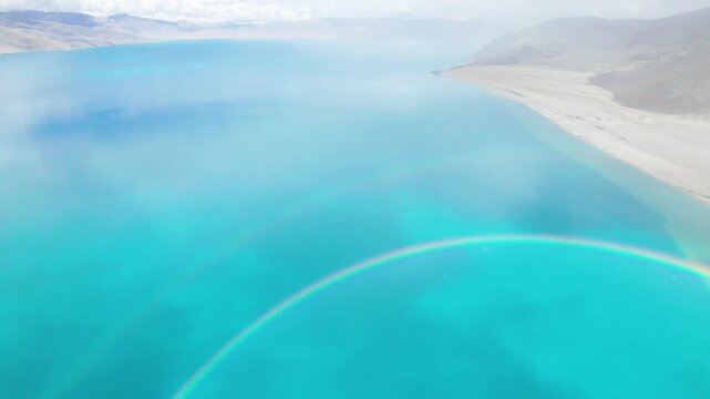 Drone view of Pegu Tso lake or Peikucuo in sunny and rainy day in Shigatse, Tibet, China, beautiful twin rainbows over peaceful turquoise sea in Xizang, 4k real time footage travel concept