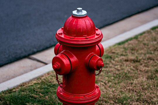 Red metal fire hydrant with chrome cap stands on grassy verge next to asphalt