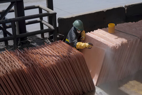 Worker Inspecting Stacks of Refined Copper Sheets at a Metal Plant