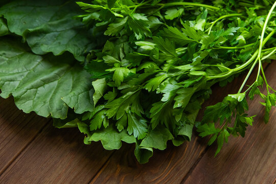Green rhubarb is arranged on a wooden table with fresh parsley and leafy greens placed nearby