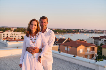 Obraz premium Middle-Aged Couple Embracing on Rooftop Terrace With Seaside View at Sunset Overlooking Marina and Town