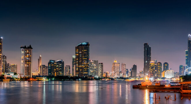 Panoramic Bangkok cityscape at night featuring illuminated skyscrapers beside Chao Phraya River. Urban architecture in Thailand modern capital. Modern waterfront architecture. Metropolitan landscape.