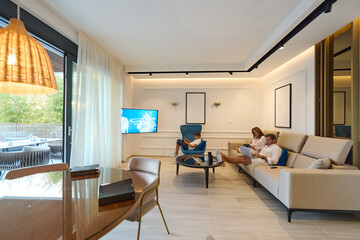 Obraz premium Family Relaxing in Modern Coastal Home Living Room With Balcony Terrace and Sea View