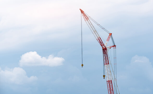 Crawler crane against blue sky and white clouds. Real estate industry. Red-white crane use reel lift up equipment in construction site. Crane for rent. Crane dealership for construction business.