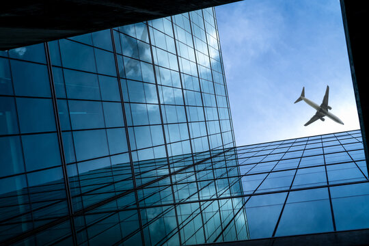 Airplane flying above modern glass office building. Perspective view of futuristic glass building. Exterior of office glass building. Business trip. Reflection in transparent glass. Company window.