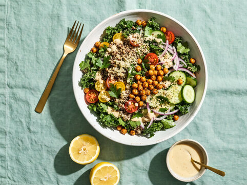 Fresh quinoa and kale salad bowl with roasted chickpeas served with creamy lemon dressing.