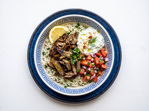 Mediterranean lamb gyro bowl with rice, tzatziki, tomatoes, and lemon wedge.