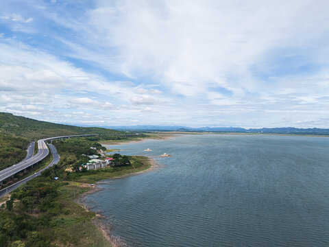 Drone aerial view of a large freshwater lake bordered by lush forest and distant mountains beneath expansive blue skies, showcasing natural landscape and tranquil scenery
