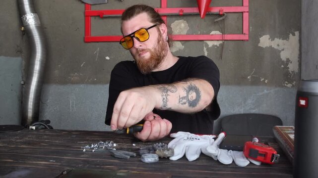 Bearded craftsman in yellow glasses cutting metal wire pieces using wire cutters in workshop