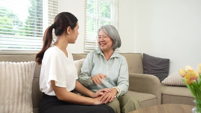 Senior woman and young caregiver enjoying a warm conversation on a sofa at home, highlighting compassionate elderly care and family support.