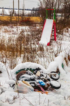 An abandoned playground with a slide, overgrown with grass and covered in snow