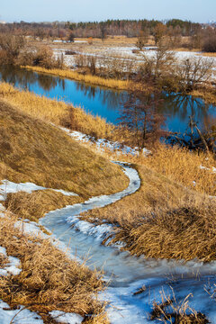 A path leads down the hill to the river. A scenic view of the countryside landscape, a sunny winter day. Snow melts on the yellow grass