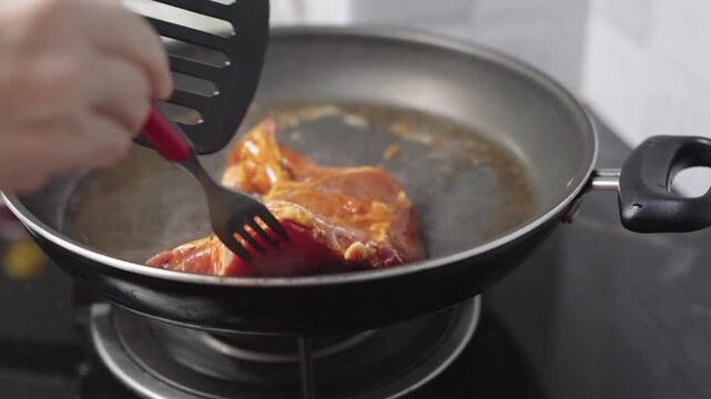 Fresh marinated meat steak frying in a hot pan on a stove with steam rising. Close-up view of cooking process at home or in a restaurant kitchen. Delicious protein meal preparation concept.