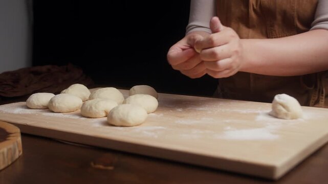 Close up of baker shaping soft dough into smooth balls by hand on a floured wooden board. Fresh homemade bread dough prepared for proofing in a rustic kitchen.