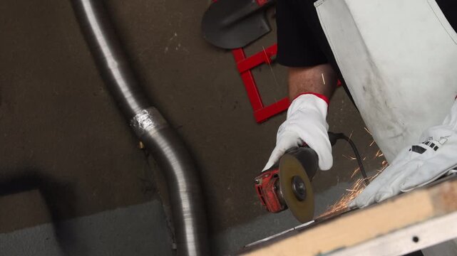Worker using power grinding tool for cutting steel plate on a workbench in a workshop