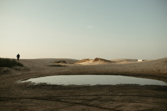 Lone man walks across desert dunes at dawn