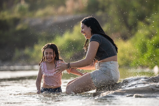 Happy mother and daughter playing and splashing in the river