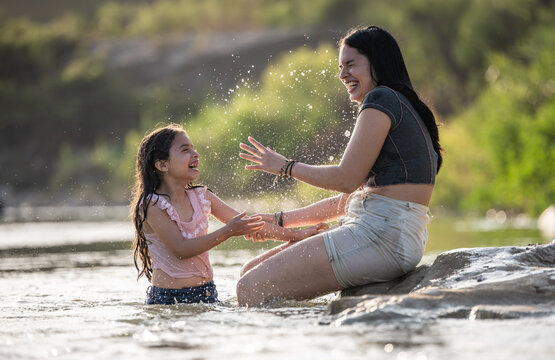 Happy mother and daughter laughing while splashing in the river