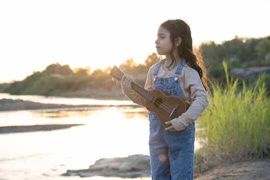Little girl holding a ukulele by a river at golden hour