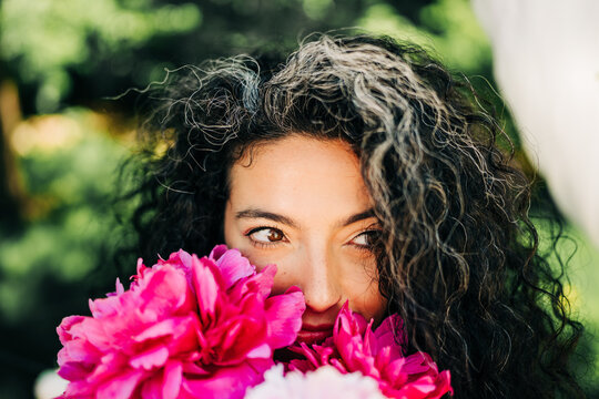 Woman with grey streak peeks over peony bouquet