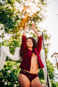 Woman with curly hair reaching for sunlight in a garden