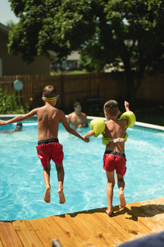 Two boys holding hands jumping into a pool during summer break