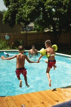 Backview of two friends holding hands jumping into a pool