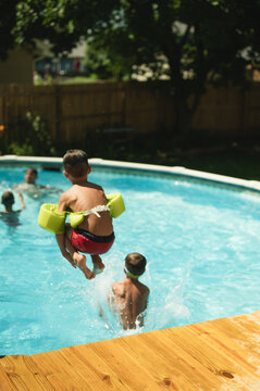 Young boy with water wings doing a cannonball jump into pool