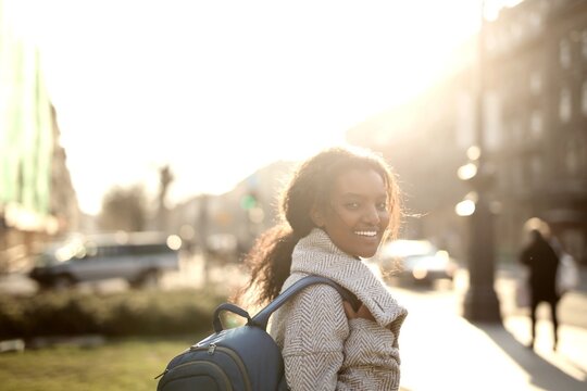 Woman looking back and smiling on a sunny city street