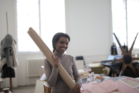 Smiling young woman holding paper roll in art studio