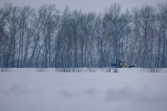 Yellow industrial tractor clearing snow near forest in winter