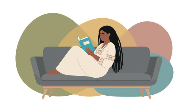 Beautiful black woman with long locs reading a book while relaxing on a comfortable grey sofa at home.