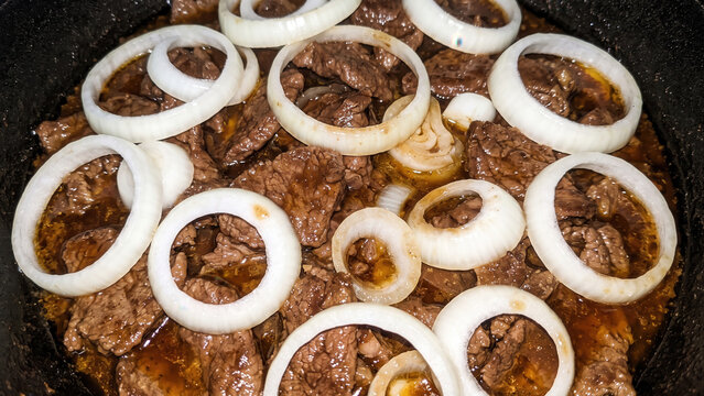Filipino beef steak topped with onion rings cooking in cast iron skillet, Bistek Tagalog 