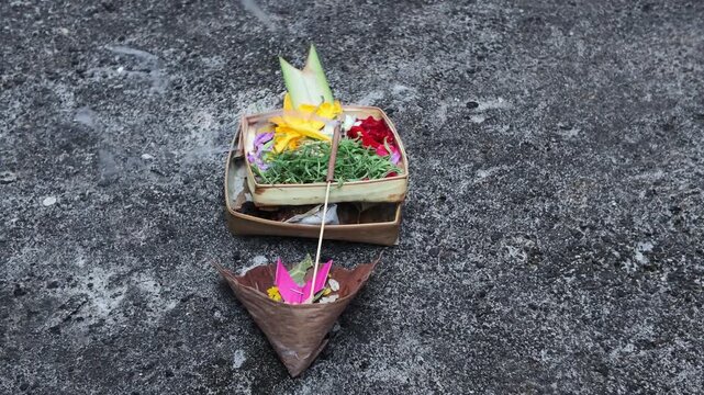 Balinese Canang Sari Offering with Burning Incense Stick on Concrete Ground