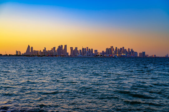 Doha modern skyline in Qatar photographed at sunset with high-rise buildings silhouetted above the Gulf waters