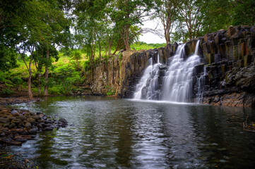 Rochester Falls in Mauritius flowing over distinctive basalt rock columns into a calm pool, surrounded by dense tropical forest and lush greenery. © Nick Fox