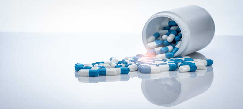 Blue-white antibiotic capsule pills spread out of plastic drug bottles. Antibiotic drug resistance. Prescription drugs. Healthcare and medicine. Pharmaceutical industry. Pharmacy product. Medication.