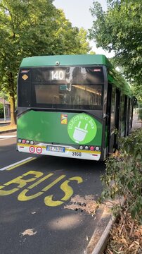 Green Electric Bus at Stop: A modern green electric bus with an illuminated route number 140 is stopped at a designated bus stop, Milan, Italy