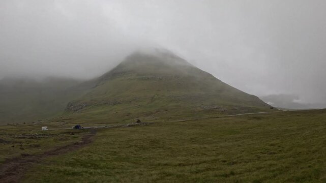 Thick fog rolling over green mountain on Eysturoy, Faroe Islands