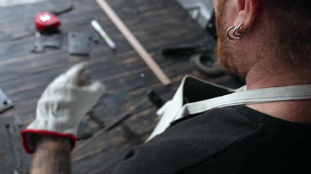 Over-the-shoulder shot of a focused craftsman preparing manual arc welding electrodes and lowering a mask in a shop