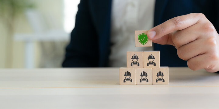 Workplace safety culture and employee protection. A green shield icon above wooden blocks with worker icons. Workplace safety, employee protection, risk prevention, compliance, and safety leadership.