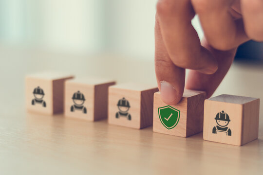 Workplace safety through employee protection concept. A hand places a safety shield among worker icons. Workplace protection, risk prevention, occupational safety, compliance, and employee wellbeing.