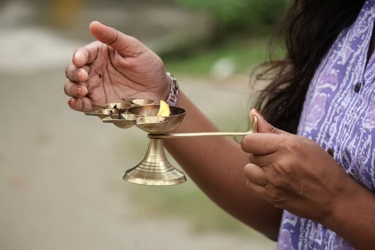 Close up of a woman holding a burning brass Panch Pradip oil lamp for a Hindu ritual