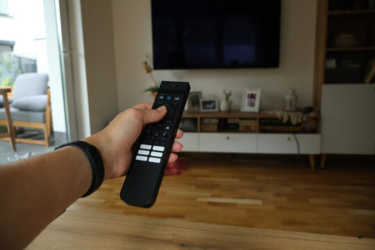 A person holding a remote control to turn on a TV. Relaxation and entertainment at home. A hand with a remote control. A person changing channels.