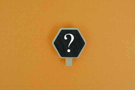​A hexagon chalkboard sign with a "QUESTION MARK" on a wooden clip against coloured background. Concept of Uncertainty, FAQ, problem-solving, and creative inquiry
