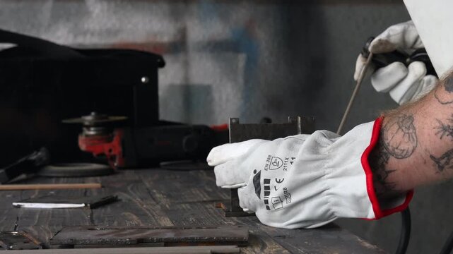 Craftsman in protective gear and mask working with welding tool on steel component