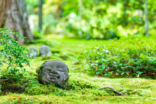 A cute little stone Jizo statue smiling on the green moss bed in a traditional Japanese garden.