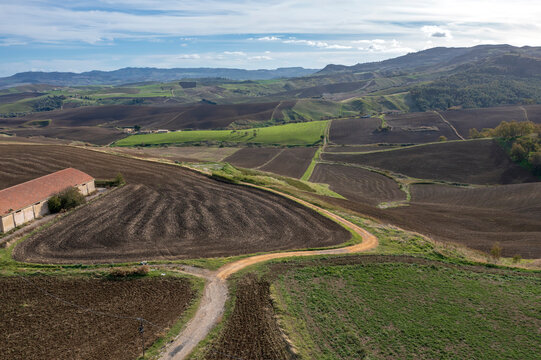 Aerial view of rolling agricultural hills with plowed fields, a country road, and an old barn