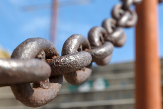 heavy rusty iron chain stretched diagonally against a blurred blue sky background