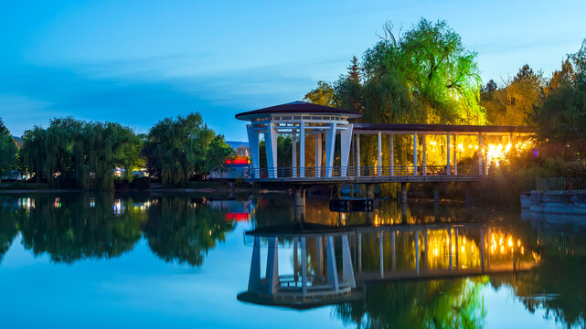 Beautiful evening view of a white lake pavilion with reflections in the still water at blue hour. Targovishte, Bulgaria